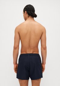Shorts de bain bleu marine avec taille élastique et poches latérales, fabriqués en matériau léger, vue de l'arrière.