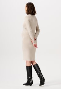 Beige jurk tot de knie met lange mouwen, aansluitend ontwerp en zachte textuur. Draagt een paar lange zwarte leren laarzen, met een gladde afwerking en een spitse neus.