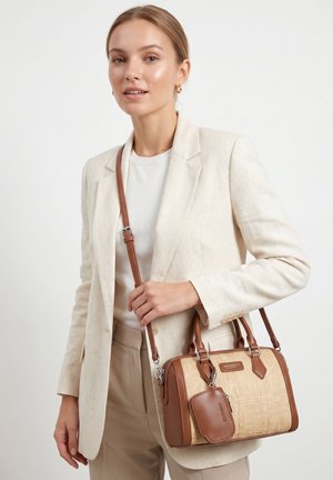 Donna con blazer e pantaloni beige porta una borsa a tracolla marrone chiaro e intrecciata con un piccolo pochetto abbinato.
