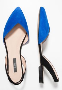 Blaue Wildleder-Slingback-Schuhe mit spitzer Zehenform, schwarzen Akzenten und flachem Absatz, ausgestattet mit einer glatten Innenauskleidung und einem kontrastierenden Design.