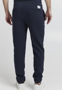 Navy blue jogger pants made of soft fabric, feature elasticated cuffs, two back pockets, and a label on the waistband.