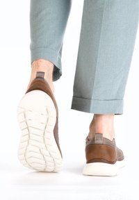 Chaussure slip-on en cuir marron et maille avec une semelle en caoutchouc blanc, dotée d'une languette à l'arrière et d'un design texturé. Portez avec un pantalon bleu clair.