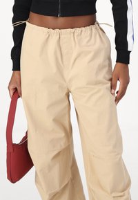 Beige wide-leg pants with an elastic waistband and drawstring detail. Smooth fabric and relaxed fit, paired with a red handbag.