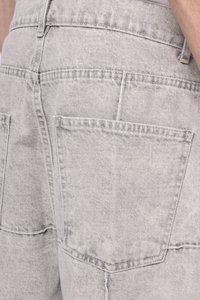 Grijze denim salopettes van textuurstof, met grote achterzakken en subtiele stikdetails, getoond vanuit een close-up achteraanzicht.