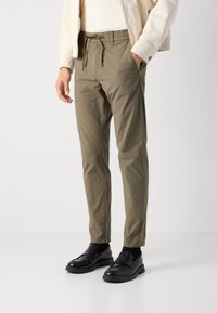 Lichte, olijfgroene broek met een elastische tailleband en trekkoord. Bevat zijzakken en een taps toelopend ontwerp. Gecombineerd met zwarte schoenen.