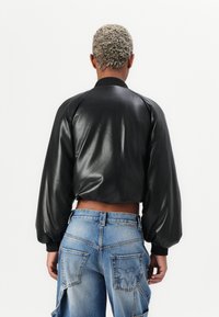Giubbotto bomber in pelle nera con maniche oversize, polsini a costine e design cropped. Abbinato a jeans in denim baggy azzurri con tasche posteriori.