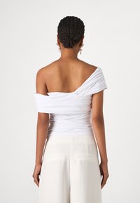 Top blanco, sin hombros, con textura fruncida, diseño ajustado y mangas cortas anchas. Llevado con pantalones de cintura alta color crema.