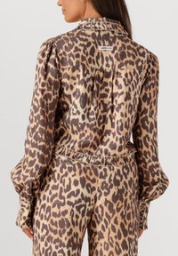 Vrouw in een beige en bruine luipaardprint blouse met lange mouwen en bijpassende broek, weergegeven vanuit de achterkant en zijaanzicht.