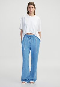 Bílý cropped top s texturovanými rukávy, doplněný o světlé modré volné kalhoty s elastickým stahovacím pasem a bočními kapsami.
