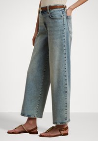 Gaiši zili džinsi ar plašu kāju un augstu jostasvietu, redzamām šuvēm; apvienoti ar brūnām siksniņām sandālēm un ribotā topā.