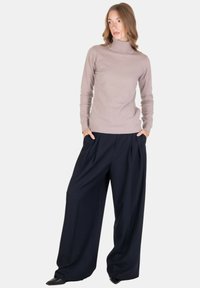 Maglione a collo alto color taupe chiaro abbinato a pantaloni a gamba larga blu navy con pieghe. Texture morbida, dettagli a coste ai polsini e in vita, design elegante.