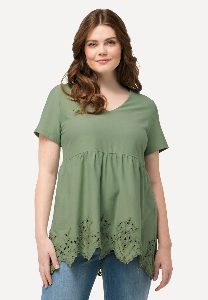 Top verde oliva de manga corta con escote en V, que presenta una cintura fruncida y detalle de ojo de perdiz bordado en el dobladillo. Textura de tela suave.