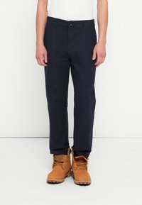 Granatowe bawełniane spodnie o prostym kroju nogawek i przednich kieszeniach, zestawione z brązowymi botkami na sznurowadła z metalowymi oczkami.