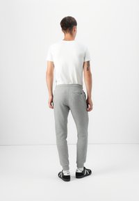 Gray athletic pants with tapered legs, elastic waistband, and side pocket, paired with a fitted white short-sleeve t-shirt and black sneakers.