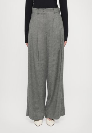Pantaloni a gamba larga plissettati in motivo houndstooth grigio, con vita aderente, passanti per cintura e una texture liscia. Abbinati a tacchi bianchi.