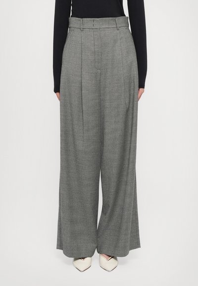 Pantaloni a gamba larga plissettati in motivo houndstooth grigio, con vita aderente, passanti per cintura e una texture liscia. Abbinati a tacchi bianchi.