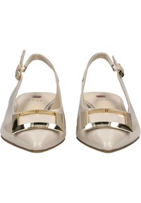 Mocasines de charol beige con tiras al tobillo y punta afilada, adornados con una hebilla geométrica en tono dorado en la parte delantera. Incluye una correa ajustable en el tobillo.