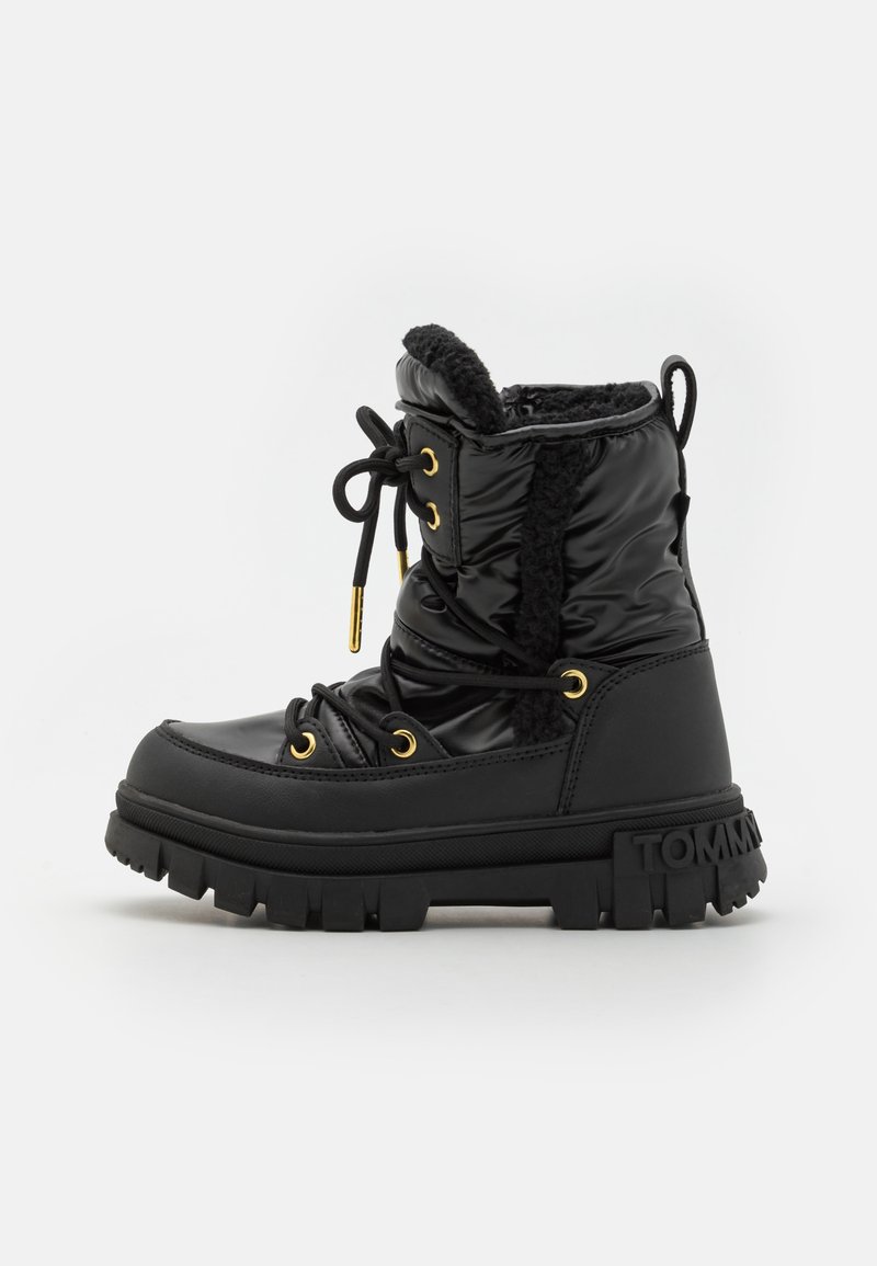 Stivaletto impermeabile nero con una texture morbida, fodera in pelliccia sintetica, dettagli in oro e una suola spessa e testurizzata. Design con lacci e dettaglio del logo.