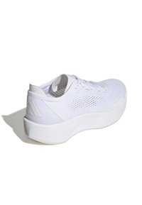 Zapatillas deportivas blancas con una parte superior de malla transpirable, cierre de cordones y una suela gruesa y texturizada. Logo en el talón, acentos suaves a los lados.