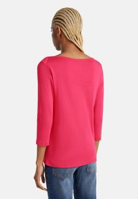 Fuchsia Oberteil mit drei Viertelärmeln und weitem Halsausschnitt, aus weichem Stoff und mit lockerer Passform, kombiniert mit hellblauen Jeans.