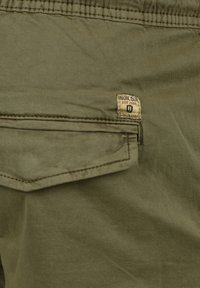 Pantalones cortos cargo en verde oliva con un bolsillo cosido, que presenta una pequeña etiqueta que dice "Indicode Est. 1993". Fabricados con una suave mezcla de algodón.