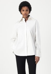 White button-up shirt with a structured collar, long sleeves, and wide cuffs. Made of smooth fabric, it features a relaxed fit and minimalistic design.