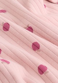 Tissu côtelé rose doux avec de petits motifs de baies rose foncé dispersés sur le matériau.
