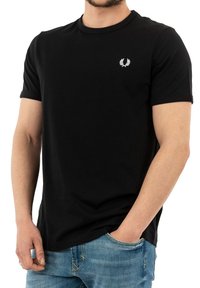 Camiseta de algodón negra de manga corta con un logotipo bordado en blanco en el lado izquierdo del pecho, combinada con unos vaqueros de color azul claro.