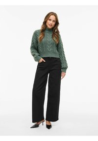 Pull cropped en tricot torsadé vert, pantalon noir à jambes larges et escarpins noirs à bout pointu. Le pull a des manches longues et un ourlet côtelé.