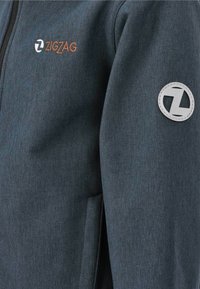Dunkelgrau zip-up Jacke mit strukturiertem Stoff, versehen mit einem orangefarbenen "ZIGZAG"-Logo und einem runden grauen Patch am Ärmel.