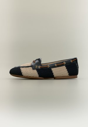 Mocassin tissé noir et crème à larges rayures, avec bordure en cuir, œillets dorés et semelle marron, vu de profil.