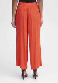 Kvinnors vida byxor i ljus orange, tillverkade av lättviktsmaterial med en strukturerad yta, med elastisk midja och en avslappnad passform.