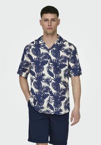Camicia a maniche corte con bottoni, caratterizzata da un motivo a foglie di palma blu navy su uno sfondo crema, realizzata in tessuto leggero.