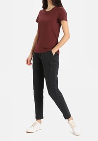 Bordová krátkosrstá tričko v kombinaci s černými cargo kalhotami s bočními kapsami, doplněné bílými teniskami. Jednoduchý, neformální outfit.