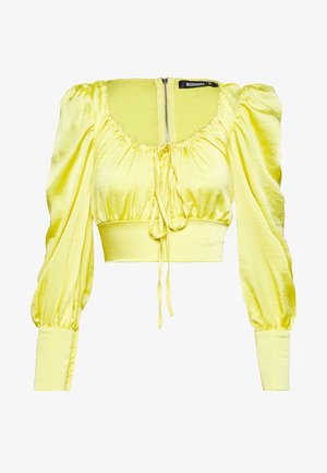 Gele satijnen cropped blouse met pofvormige lange mouwen, geplooide halslijn met centrale trekkoord, brede aangesloten tailleband en ritssluiting aan de achterkant.