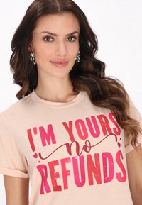 Lyserød kortærmet t-shirt med fed rød og lyserød tekst, der står "JEG ER DIN ingen REFUND", med dekorative detaljer. Blød tekstur.