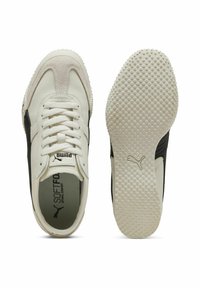Zapatillas blancas de cuero con acentos negros, puntera redonda, suela con textura antideslizante, cordones planos y detalle de logo en la lengüeta y el costado.