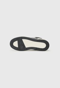 Zwarte rubberen sneakerzool met textuurpatronen, verhoogde accenten en een contrasterende beige streep. Heeft een ronde indruk op de hiel.