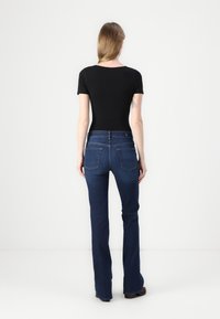 Body corto nero a maniche corte e jeans svasati blu scuro con tasche posteriori. Tessuto liscio; design aderente; cuciture pulite; dettagli minimi.