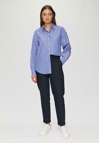 Blau-weißer gestreifter Button-Down-Hemd mit Kragen, kombiniert mit dunklen Hosen und weißen Sneakers. Glattes Material, lässige Passform.