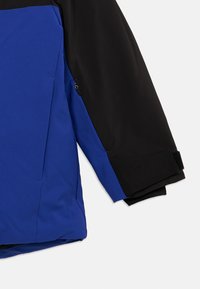 Μπλε και μαύρο μπουφάν με μανίκι και λεπτομέρεια φερμουάρ, καθώς και ρυθμιζόμενο βέλκρο μαύρο λουράκι στον καρπό, απεικονίζεται σε λευκό φόντο.