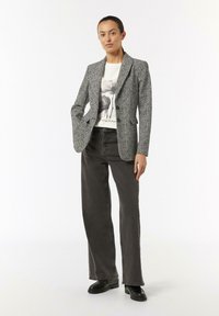 Marynarka w wzór houndstooth w czerni i bieli, zestawiona z koszulą z grafiką i ciemnymi dżinsami o wysokim stan. Stylizowana z masywnymi czarnymi butami.