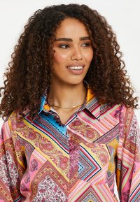 Farverig mønsteret skjorte med paisley- og geometriske designs, med knap-ned krave og lange ærmer. Stoffet ser let og struktureret ud.