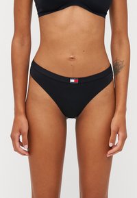 Čierne bavlnené bikiny s úzkym pásom a malým logom v červenej, bielej a modrej farbe vpredu. Hladká textúra.