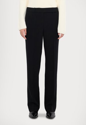 Pantalon noir ajusté avec un design à jambe droite et une texture lisse. Comprend des passants de ceinture et une taille nette. Assorti à un pull crème.