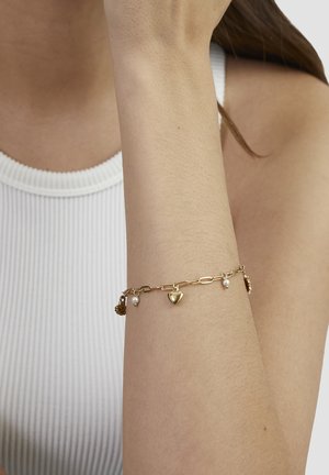 Gold chain bracelet with charms, including a heart and pearls, on a wrist. Features links and delicate hardware detail.