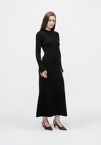 Černé šaty s dlouhým rukávem z měkké látky, s přiléhavým střihem, kulatým výstřihem a jemnou žebrovanou texturou. Nosit s lodičkami s špičatou špičkou.