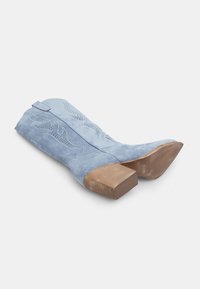 Ljusblå mocka cowboystövlar med fyrkantig klack, med sydda vågmönster och dekorativa perforeringar på skaftet.