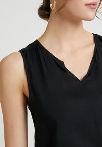 Black sleeveless top with a V-neck design, featuring soft fabric and subtle gathering at the shoulder seams for added texture.