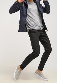 Marinblå vattentät jacka med små vita prickar, grå randig skjorta, svarta slim-fit byxor och ljusgrå slip-on skor med vita sulor.